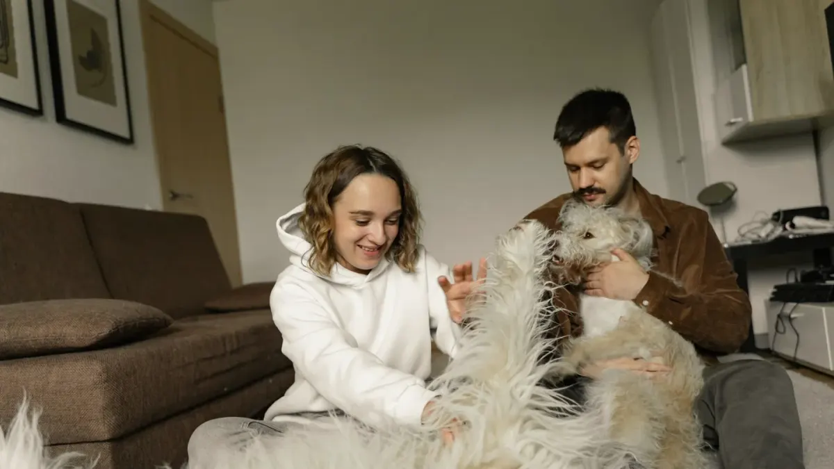 A dog owner sitting on the floor with a nervous dog while a professional takes notes nearby