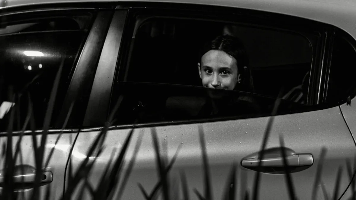 A dog sitting low in the backseat of a car, looking anxious near the window
