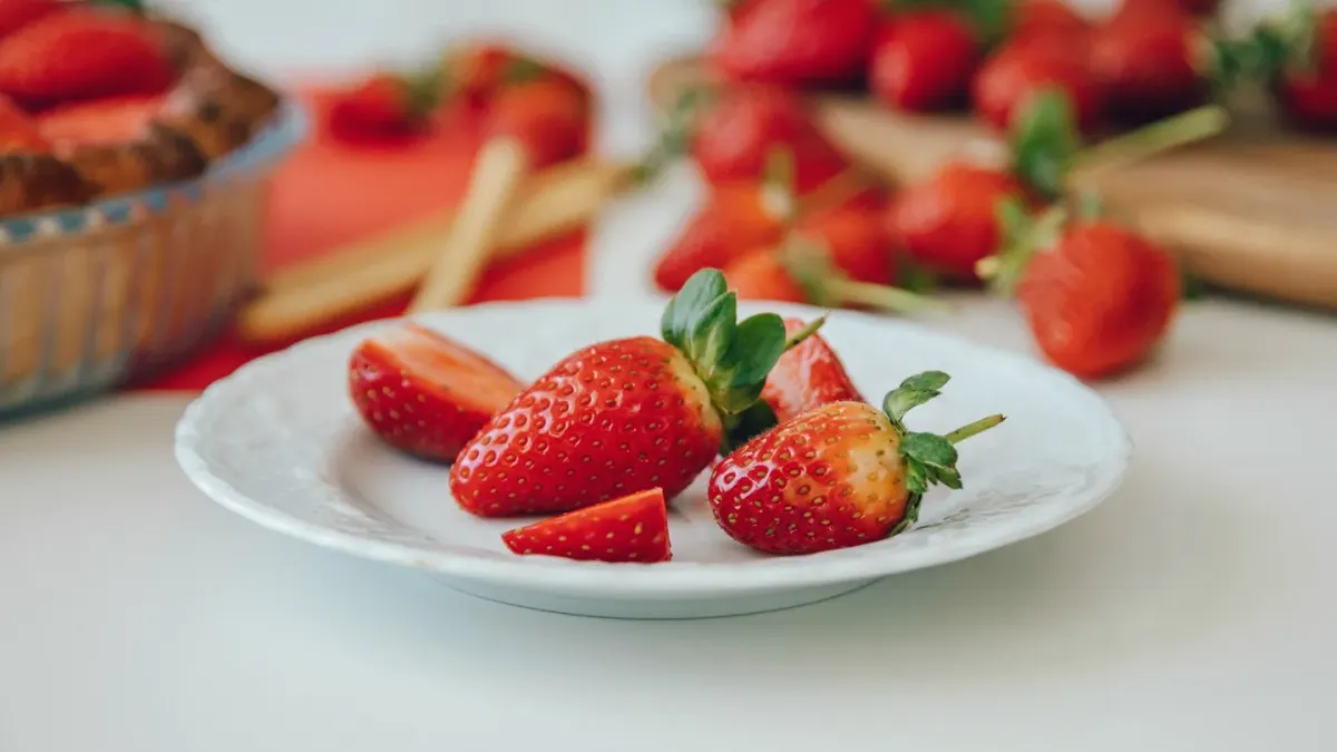 A dog sniffing a small bowl of sliced fresh strawberries on a kitchen counter