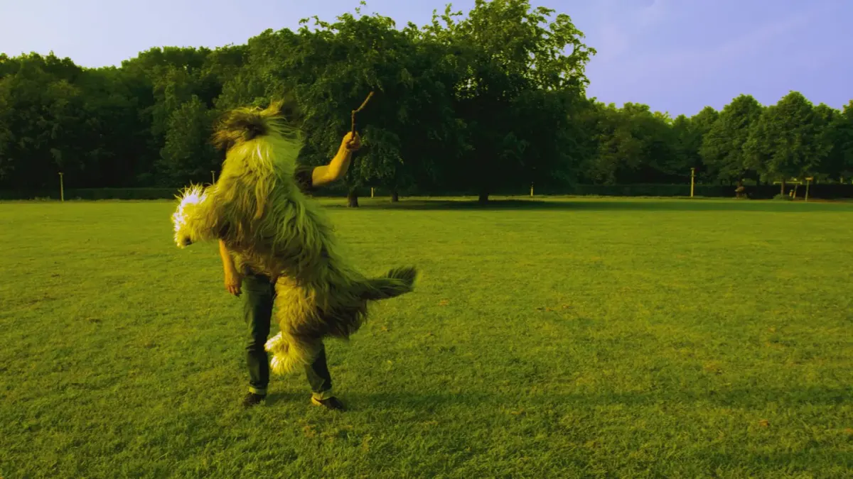 A dog sprinting across an open grassy field with its owner in the distance