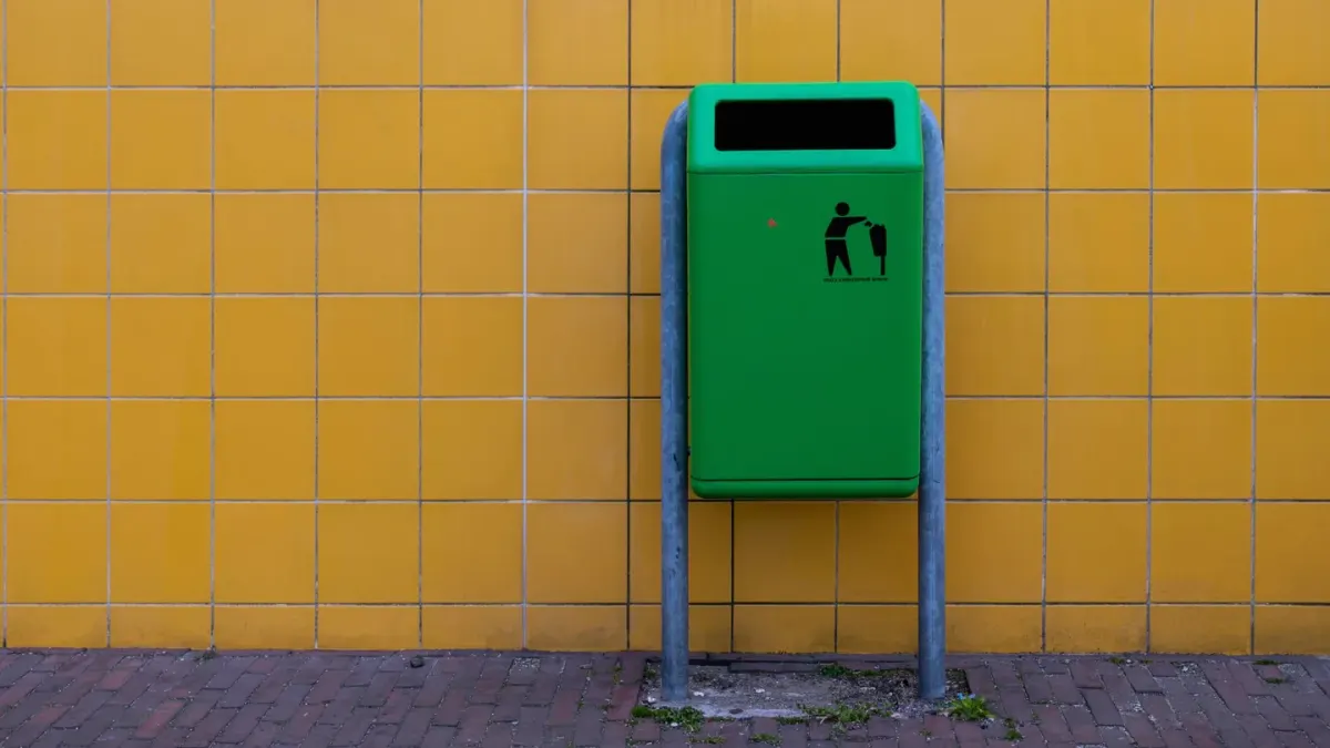A dog standing beside an open kitchen trash can with its nose inside