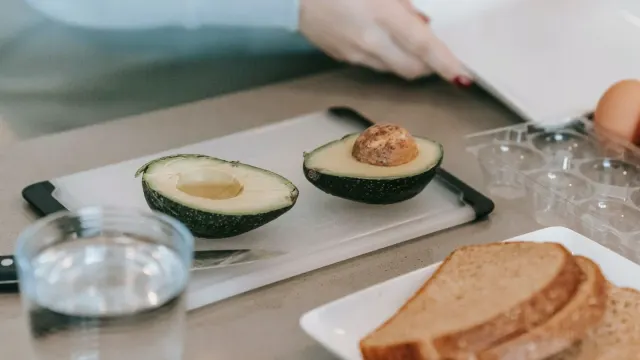 A halved avocado on a cutting board while a dog watches nearby