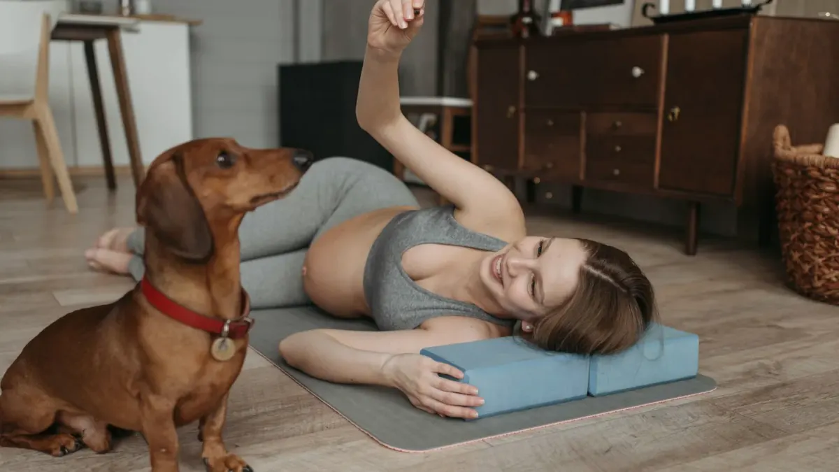 A person kneeling beside a dog on a mat, gently supporting and flexing the dog's hind leg