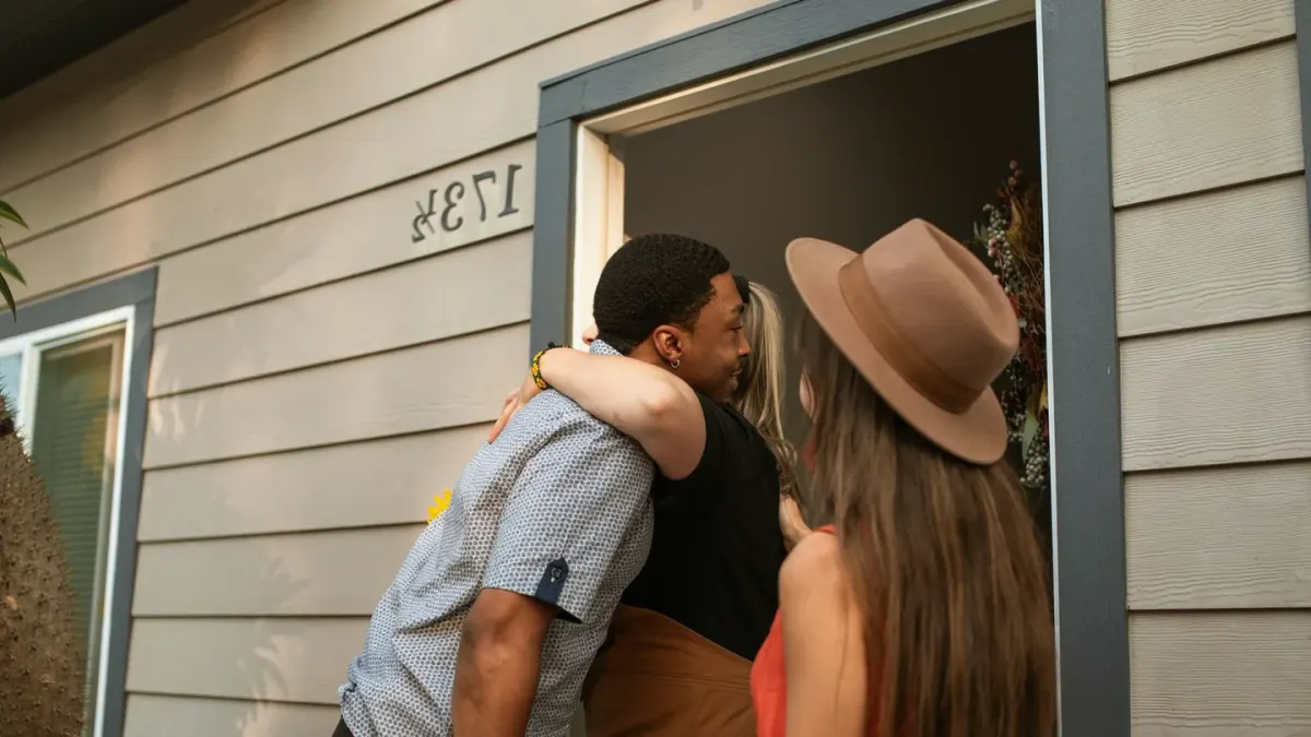 A pet sitter kneeling down to greet a senior dog at the front door of a house