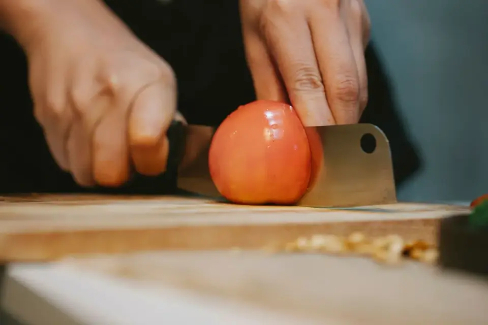 A ripe red tomato slice on a wooden cutting board beside an empty dog bowl