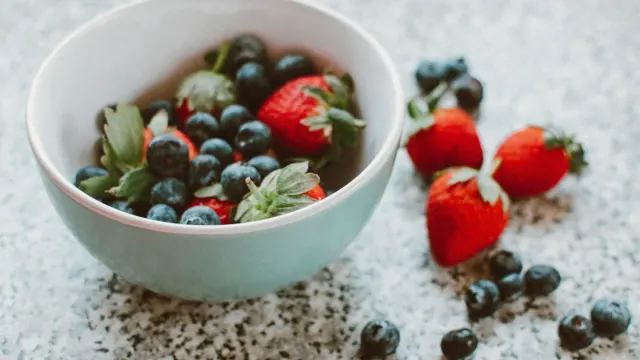 A small bowl of fresh blueberries on a kitchen floor next to a golden retriever