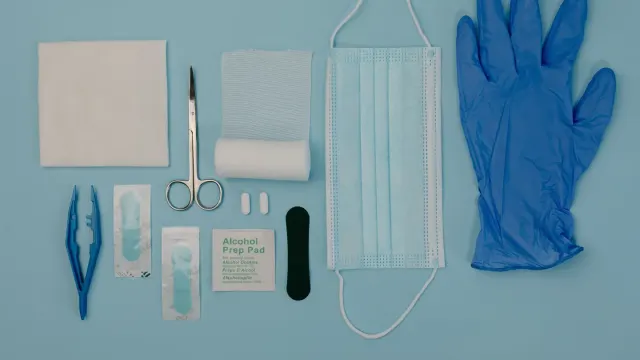 A small first-aid kit with gauze, tape, and a thermometer laid out beside a dog travel carrier