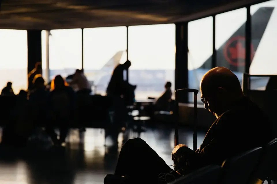 A traveler holding pet travel documents next to a dog carrier at an airport