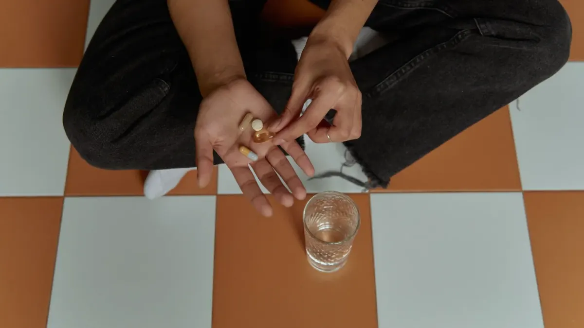 A woman's hand holding an open probiotic supplement capsule next to a small dog resting on a kitchen floor