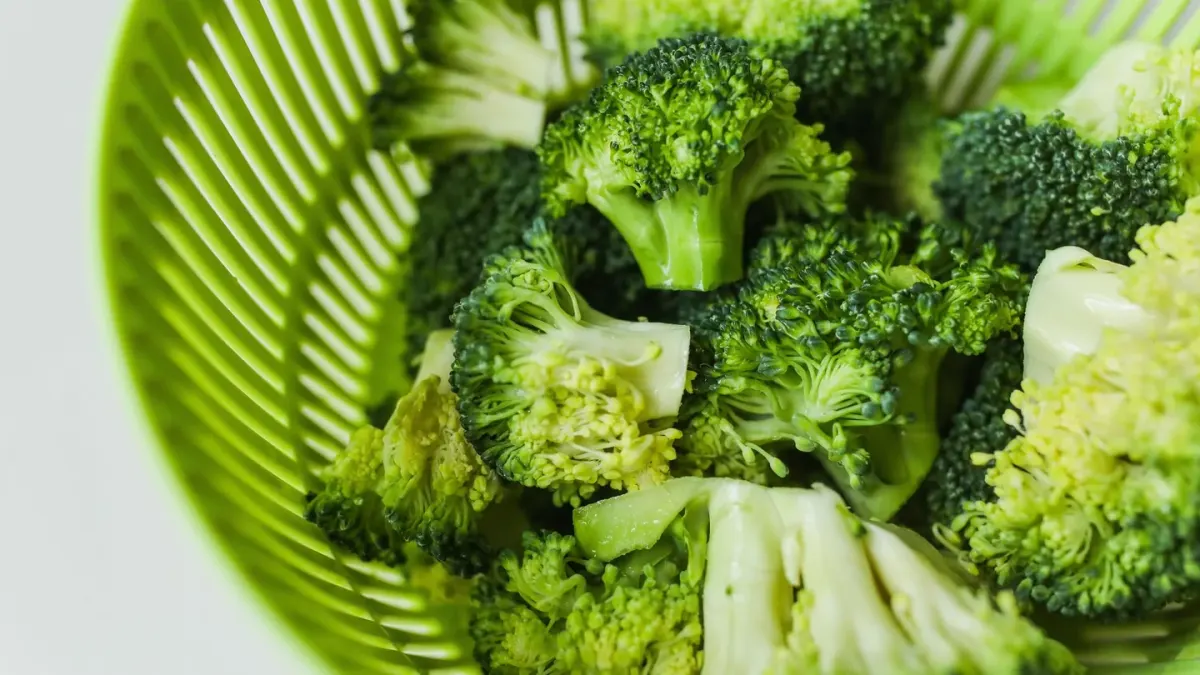 Raw broccoli florets on a cutting board with a dog watching nearby