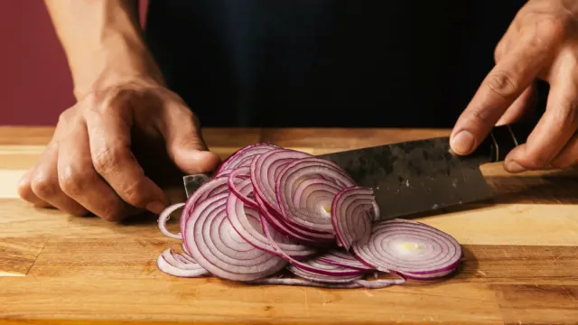 Sliced onions on a wooden cutting board beside an empty dog bowl